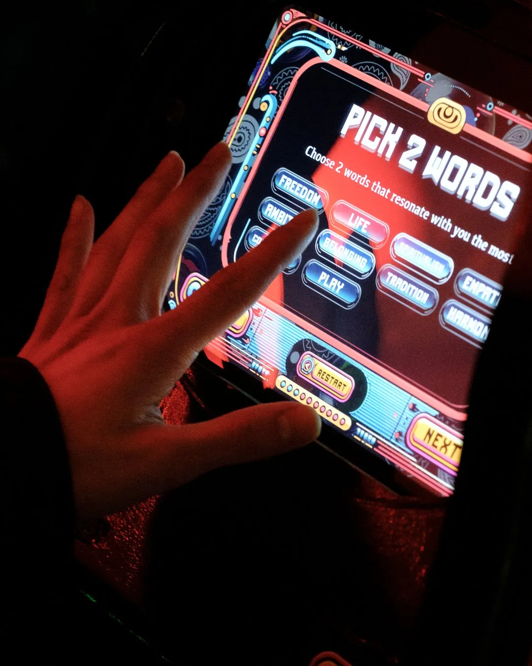 A hand on an AFTM touchscreen that reads Pick 2 Words
